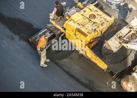 Lavoratori deporre un nuovo rivestimento in asfalto utilizzando bitume caldo. Lavoro di macchinari pesanti e lastricatore. La vista dall'alto Foto Stock