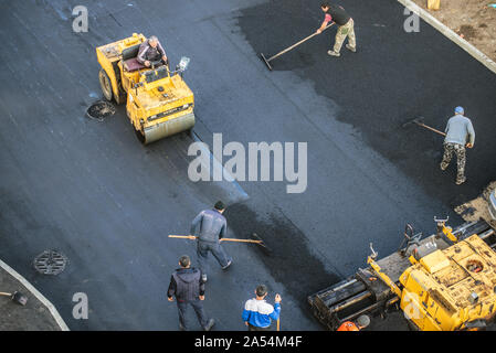 Lavoratori deporre un nuovo rivestimento in asfalto utilizzando bitume caldo. Lavoro di macchinari pesanti e lastricatore. La vista dall'alto Foto Stock