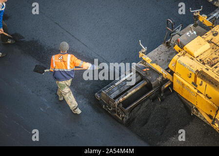 Lavoratori deporre un nuovo rivestimento in asfalto utilizzando bitume caldo. Lavoro di macchinari pesanti e lastricatore. La vista dall'alto Foto Stock