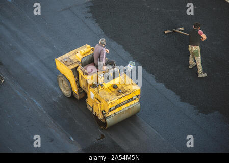 Lavoratori deporre un nuovo rivestimento in asfalto utilizzando bitume caldo. Lavoro di macchinari pesanti e lastricatore. La vista dall'alto Foto Stock