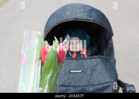 Fiori giovani madri. Felice Festa della mamma di un bambino piccolo si congratula con le mamme e dà i suoi fiori di tulipani rossi. Rendimento di grazie per il bambino. Foto Stock