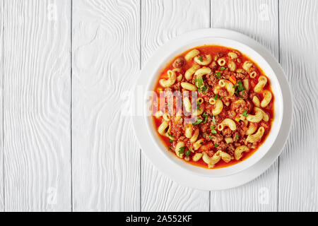 Classic american gulasch di gomito pasta, carni bovine, il sedano e i pomodori in una ciotola bianco su bianco di un tavolo di legno, vista da sopra, flatlay, spazio libero Foto Stock