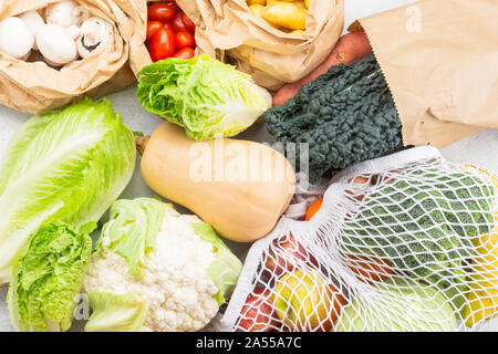 Assortimento di frutta verdura riutilizzabili in maglia bianca, cotone e sacchi di carta bianca sul tavolo da cucina, vista dall'alto, il fuoco selettivo Foto Stock