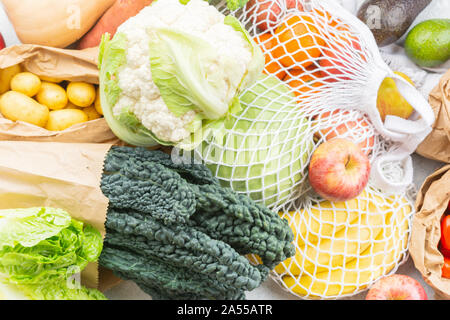 Assortimento di frutta verdura riutilizzabili in maglia bianca, cotone e sacchi di carta bianca sul tavolo da cucina, vista dall'alto, il fuoco selettivo Foto Stock