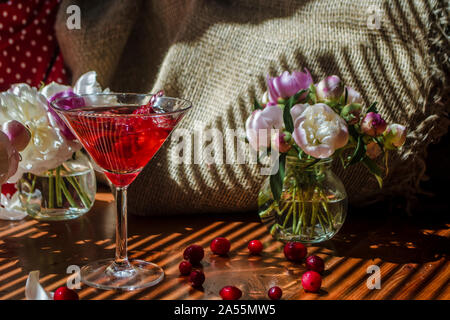 Solenne ancora in vita con un bicchiere di rosso a bere con autunno bacche con uno splash e schizza di caduta di berry circondato da fiori bianchi sul retro tessile Foto Stock