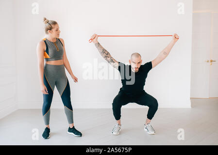 Donna osservando istruttore di fitness utilizzando la banda di resistenza in studio Foto Stock