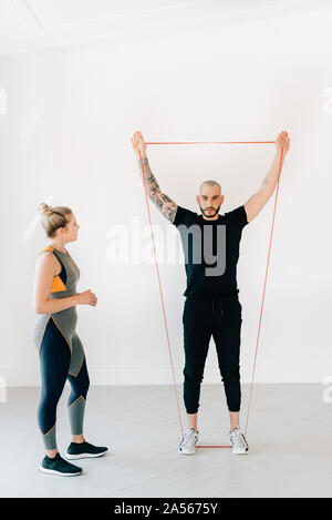 Donna osservando istruttore di fitness utilizzando la banda di resistenza in studio Foto Stock