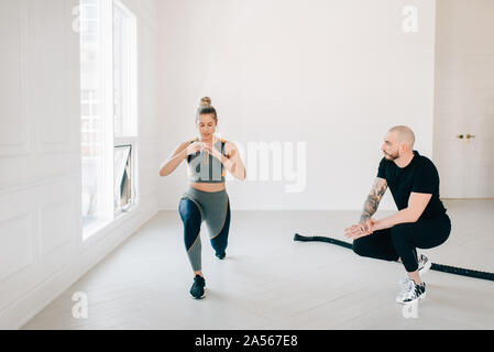 Istruttore di Fitness osservando la donna facendo balzi in avanti in studio Foto Stock