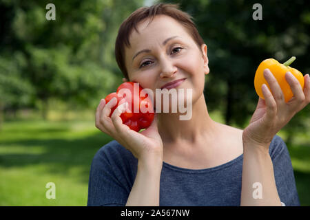 Donna di mezza età sorridente e tenendo il peperone paprika. Uno stile di vita sano concetto. Mangiare sano. Vegetariano. Paleo dieta. Cibo sano. Foto Stock