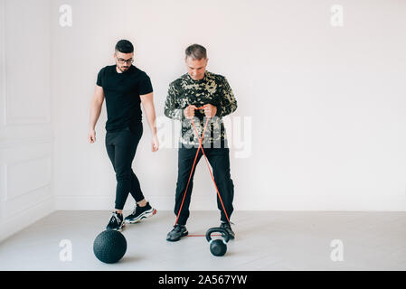 Istruttore di Fitness osservando l'uomo utilizzando la banda di resistenza in studio Foto Stock