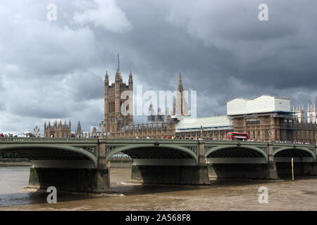 Westminster Bridge con il Parlamento, le nuvole scure e red London bus Foto Stock