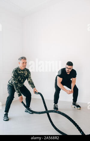 Istruttore di Fitness osservando l'uomo utilizzando la battaglia di corda in studio Foto Stock