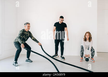 Istruttore di Fitness osservando l'uomo utilizzando la battaglia di corda in studio Foto Stock