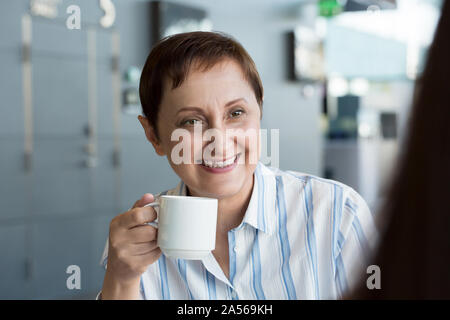 Donna anziana a parlare con il suo collega. Donna con un incontro con un partner aziendale o un cliente. Ritratto di mezza età femmina presentando un caffè / tè Foto Stock