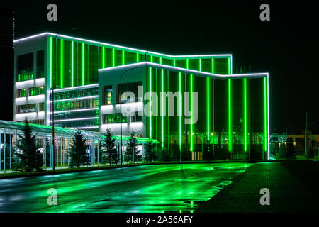 Moderno edificio di tech incorniciato da una linea verde di luci al neon. Un ammaliante vista della città di notte con la riflessione di luci al neon su strada bagnata. Foto Stock