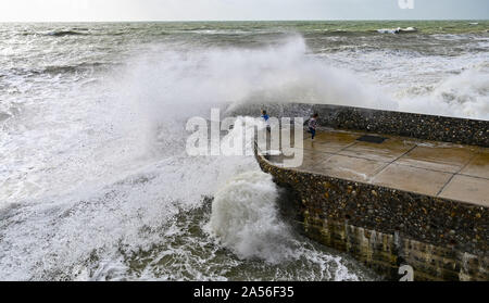 Brighton Regno Unito 18 ottobre 2019 - Visitatori coperti di sea spray come le onde in crash sul lungomare di Brighton come una miscela di venti forti rovesci di pioggia e sole sweep lungo la costa del sud come le perturbazioni atmosferiche continua in tutta la Gran Bretagna . Credito: Simon Dack / Alamy Live News Foto Stock