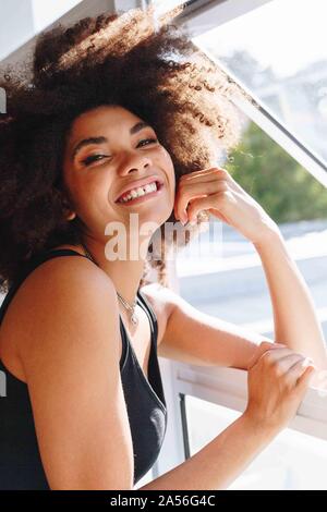 Felice giovane donna con acconciatura afro presso la finestra della camera, la testa e la spalla verticale Foto Stock