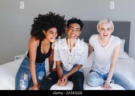 Giovane uomo e due amiche seduta sul letto ridendo Foto Stock