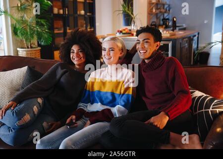 Felice metà uomo adulto e giovani amici di sesso femminile di guardare la TV sul divano di casa Foto Stock