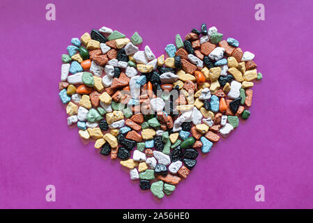 Il concetto di amore.a forma di cuore decorazione da ciottoli colorati su uno sfondo viola.choco rocce appare come ciottoli.close up. Foto Stock
