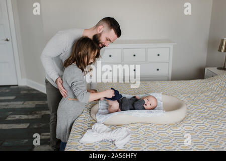 Ragazza con padre modifica baby fratello del pannolino sul letto, vista laterale Foto Stock