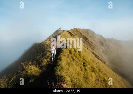 Giovane femmina escursioni turistiche sulla cima della montagna nebbioso, vista posteriore, Bali, Indonesia Foto Stock
