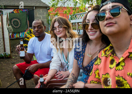 Quattro giovani amici adulti in un momento di relax a comunità party in giardino, vista laterale verticale Foto Stock