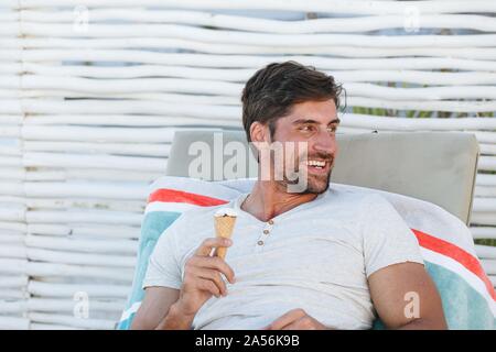 L'uomo godendo di cono gelato sulla sedia a sdraio Foto Stock