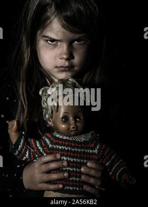 Foto di un inquietante ragazza giovane con una vecchia bambola per tema Halloween. Foto Stock