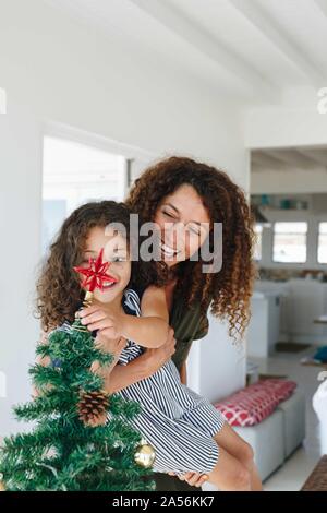 Madre aiutare mia figlia stella posto su albero di Natale a casa Foto Stock