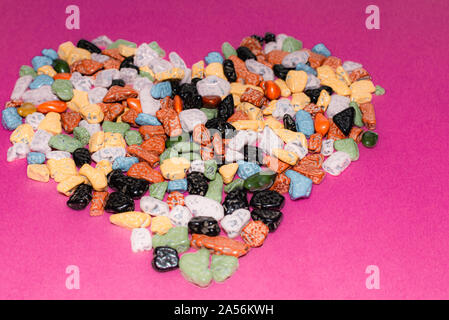 Il concetto di amore.a forma di cuore decorazione da ciottoli colorati su un sfondo rosa.choco rocce appare come ciottoli.close up. Foto Stock