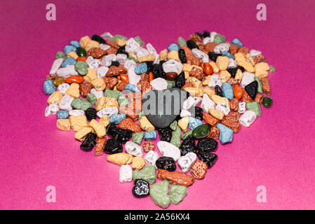 Il concetto di amore.a forma di cuore decorazione da ciottoli colorati su un sfondo rosa.choco rocce appare come ciottoli.close up. Foto Stock