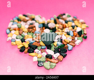 Il concetto di amore.a forma di cuore decorazione da ciottoli colorati su un sfondo rosa.choco rocce appare come ciottoli.close up. Foto Stock