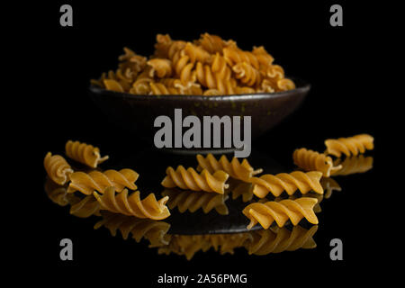Sacco di tutto il marrone e secca fusilli integrali in scuro vaso in ceramica isolata sul vetro nero Foto Stock