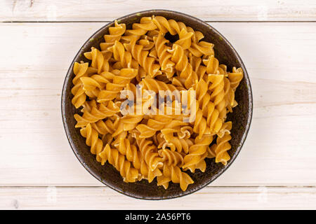 Sacco di tutto il marrone e secca fusilli integrali in ceramica scura flatlay ciotola in legno di colore bianco Foto Stock