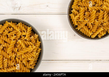 Sacco di tutto il marrone e secca fusilli integrali in ceramica scura la ciotola in ceramica grigia flatlay ciotola in legno di colore bianco Foto Stock