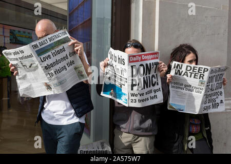 Gli attivisti ambientali leggere le copie di un fake giornale con fictional della notizia circa gli effetti del cambiamento climatico globale durante una occupazione di Oxford Circus a Londra centrale, parte di due settimane di prolungate proteste in tutto il mondo dai membri di estinzione della ribellione, il 18 ottobre 2019, a Londra, in Inghilterra. Foto Stock