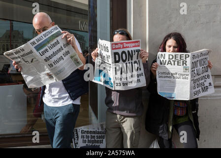 Gli attivisti ambientali leggere le copie di un fake giornale con fictional della notizia circa gli effetti del cambiamento climatico globale durante una occupazione di Oxford Circus a Londra centrale, parte di due settimane di prolungate proteste in tutto il mondo dai membri di estinzione della ribellione, il 18 ottobre 2019, a Londra, in Inghilterra. Foto Stock