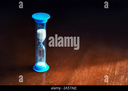La clessidra di colore blu con sabbia bianca su sfondo scuro Foto Stock