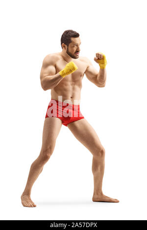 A piena lunghezza shot forte di un giovane uomo in pantaloncini rossi esercizio di kickboxing isolati su sfondo bianco Foto Stock