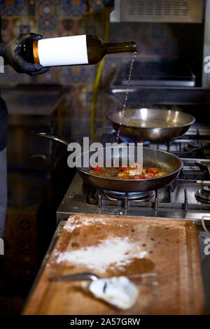 Concetto di cibo. Lo chef versa vino bianco friggere in una padella i pomodori e le ostriche. Il processo di cottura di spaghetti con frutti di mare. Foto Stock