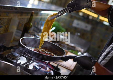 Concetto di cibo. Lo chef aggiunge spaghetti friggere in una padella i pomodori e le ostriche. Il processo di cottura di spaghetti con frutti di mare. Foto Stock