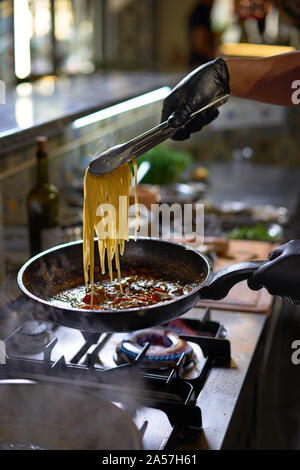 Concetto di cibo. Lo chef aggiunge spaghetti friggere in una padella i pomodori e le ostriche. Il processo di cottura di spaghetti con frutti di mare. Foto Stock
