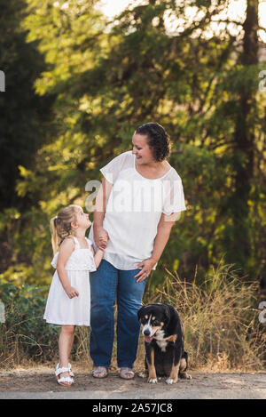 Ragazza giovane e sorridente mom a vicenda con la famiglia pup ai loro piedi Foto Stock