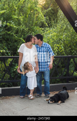 Giovane ragazza ridere come genitori bacio sul ponte con cane a piedi Foto Stock