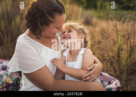 Dai capelli scuri di coccole mom sorridente giovane figlia all'aperto su quilt Foto Stock