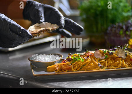 Concetto di cibo. Lo chef aggiunge alla pasta, ostrica fresca su una piastra. Il processo per la fabbricazione di spaghetti con frutti di mare. Messa a fuoco selettiva. Profondità del fie Foto Stock