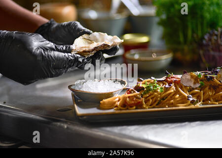 Concetto di cibo. Lo chef aggiunge alla pasta, ostrica fresca su una piastra. Il processo per la fabbricazione di spaghetti ai frutti di mare.Il fuoco selettivo. Profondità di fiel Foto Stock