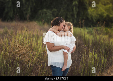 A piedi nudi 4 anni whispering in mom l orecchio nel campo erboso Foto Stock