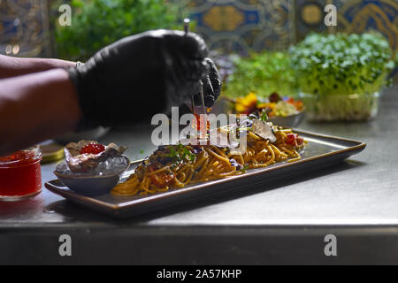 Concetto di cibo. Lo chef contorni con caviale rosso un pesce piatto di spaghetti. Messa a fuoco selettiva. Profondità di campo. Foto Stock